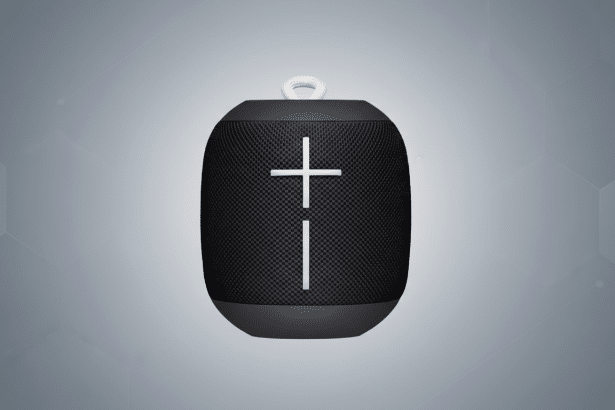 A professional shot of a black portable speaker with volume controls on the front, set against a subtle , light gray geometric pattern background. Filename : black portablespeaker . png