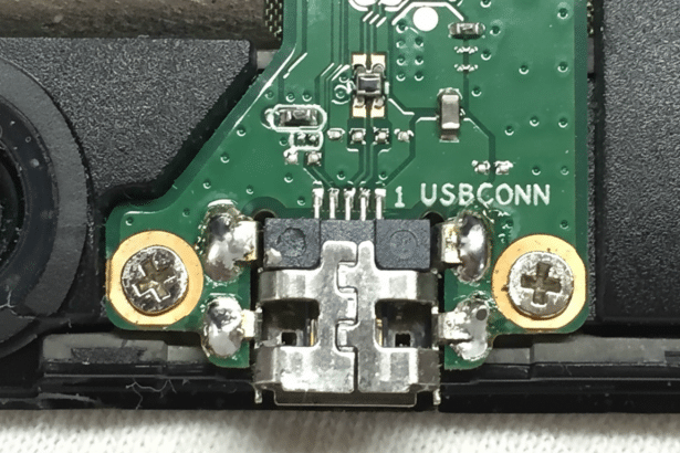 Close- up of a green circuit board with a USB connector labeled 1 US BCONN and two visible screws, set against a dark background.