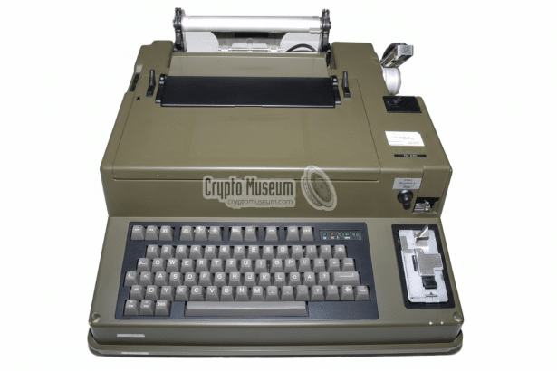 A vintage olive green tele printer machine with a QW ERTZ keyboard and a paper roll mechanism on top, set against a plain white background. Filename : vintage teleprinter 16x 9.png