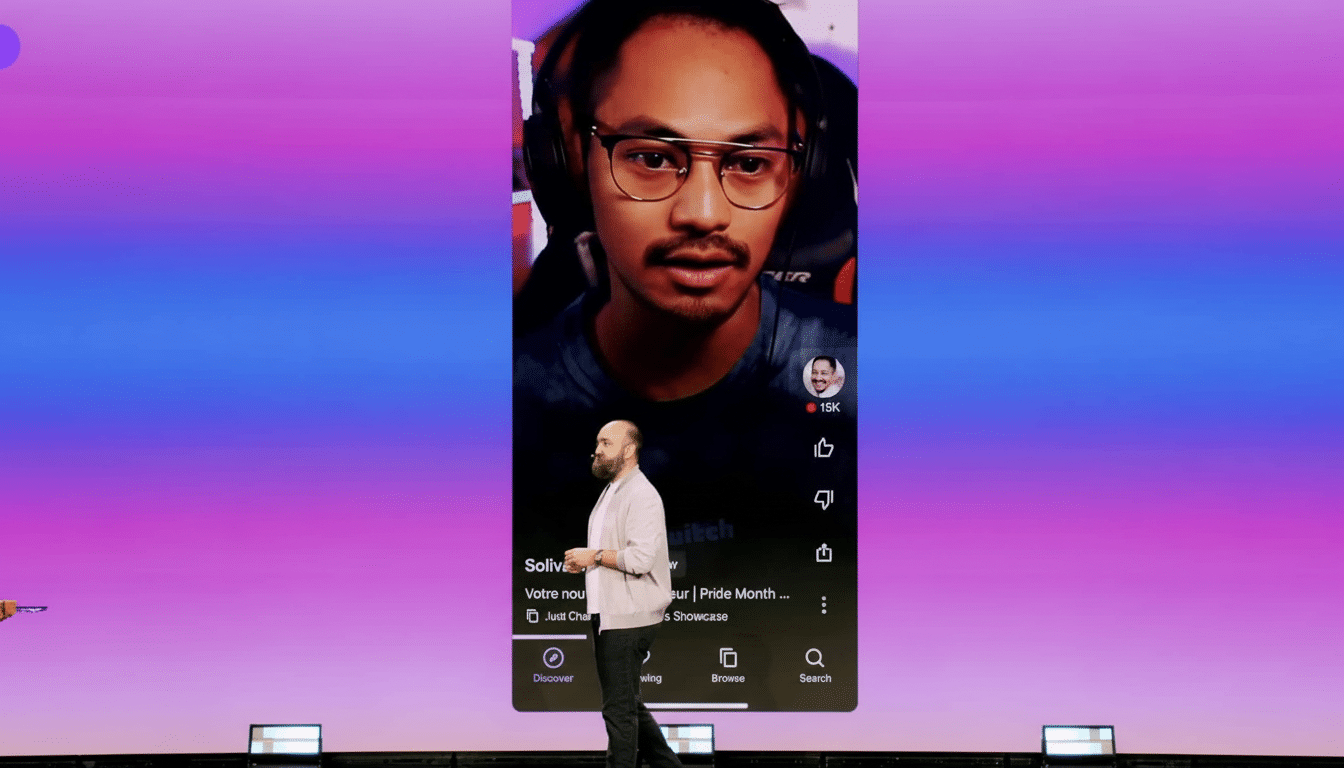 A man standing on a stage in front of a giant screen displaying a vertical video of another man wearing headphones. The screen has a purple and blue gradient background.