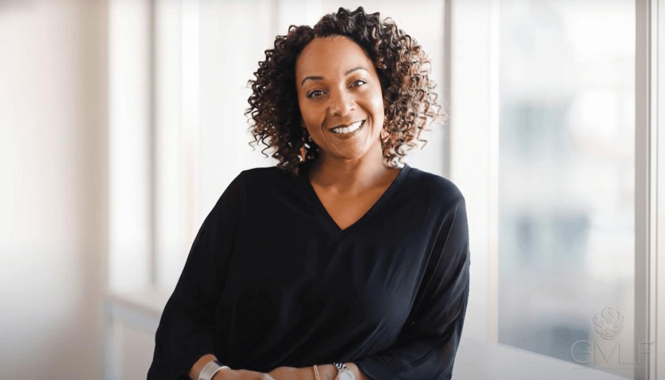 A smiling woman with curly hair wearing a black top, professionally enhanced and resized to 16: 9 aspect ratio.