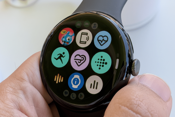 A close -up shot of a Google Pixel Watch being held, displaying various colorful app icons on its circular screen, including icons for fitness tracking , heart rate, and notifications .