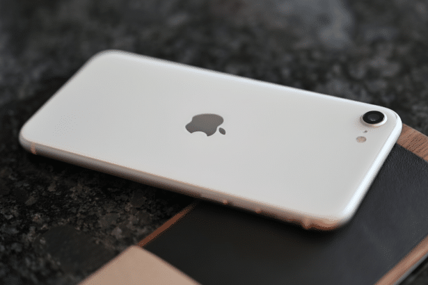 White iPhone with the Apple logo visible on the back, resting on a dark, textured surface with a wooden and leather notebook.