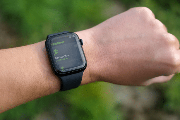 A close -up shot of a persons wrist wearing an Apple Watch, displaying the Workout app with Outdoor Run selected and OPEN GOAL visible. The background