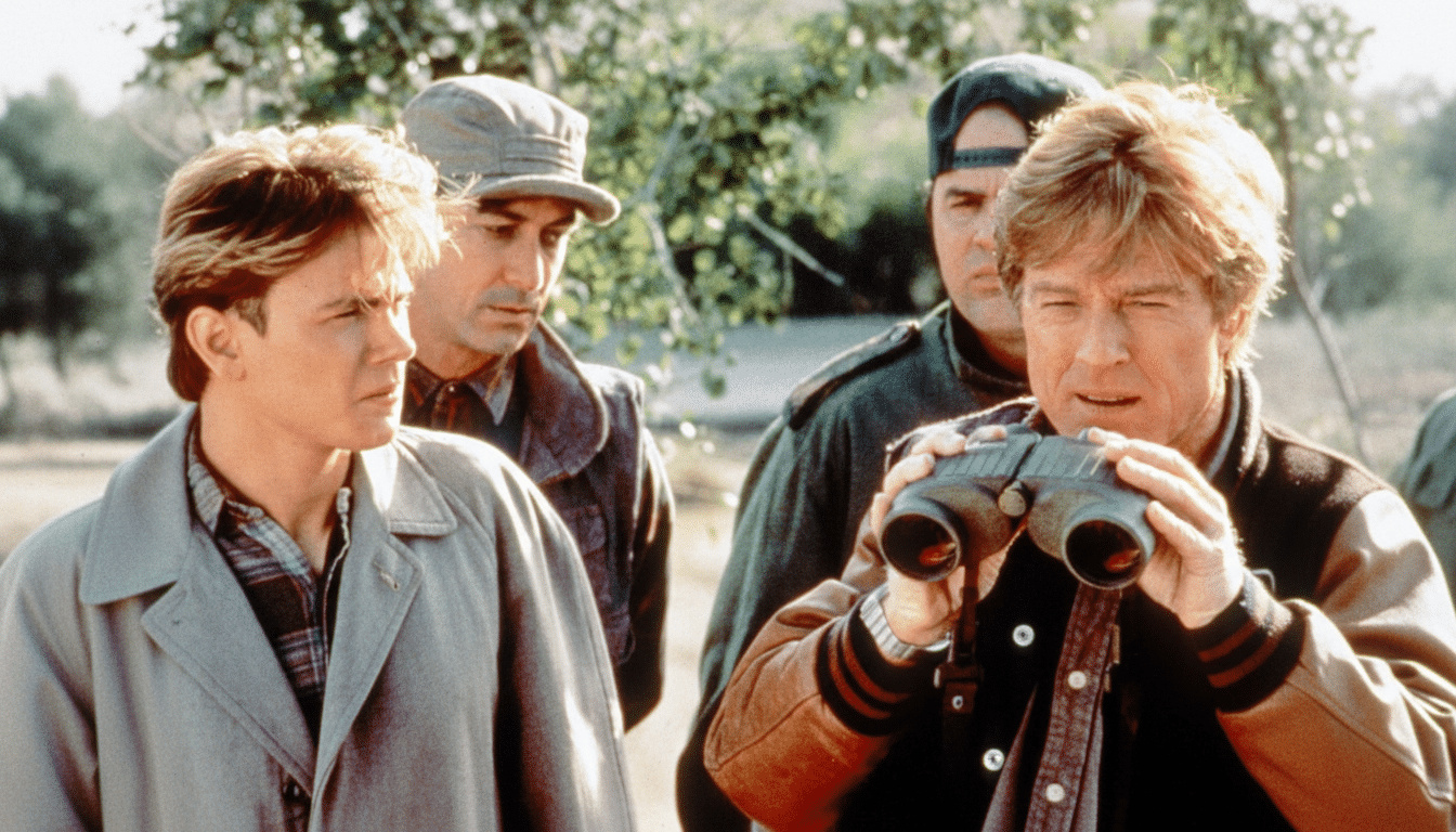 Four men outdoors, with one man in the foreground using binoculars, and another man to his left looking intently . Two other men are in the background.