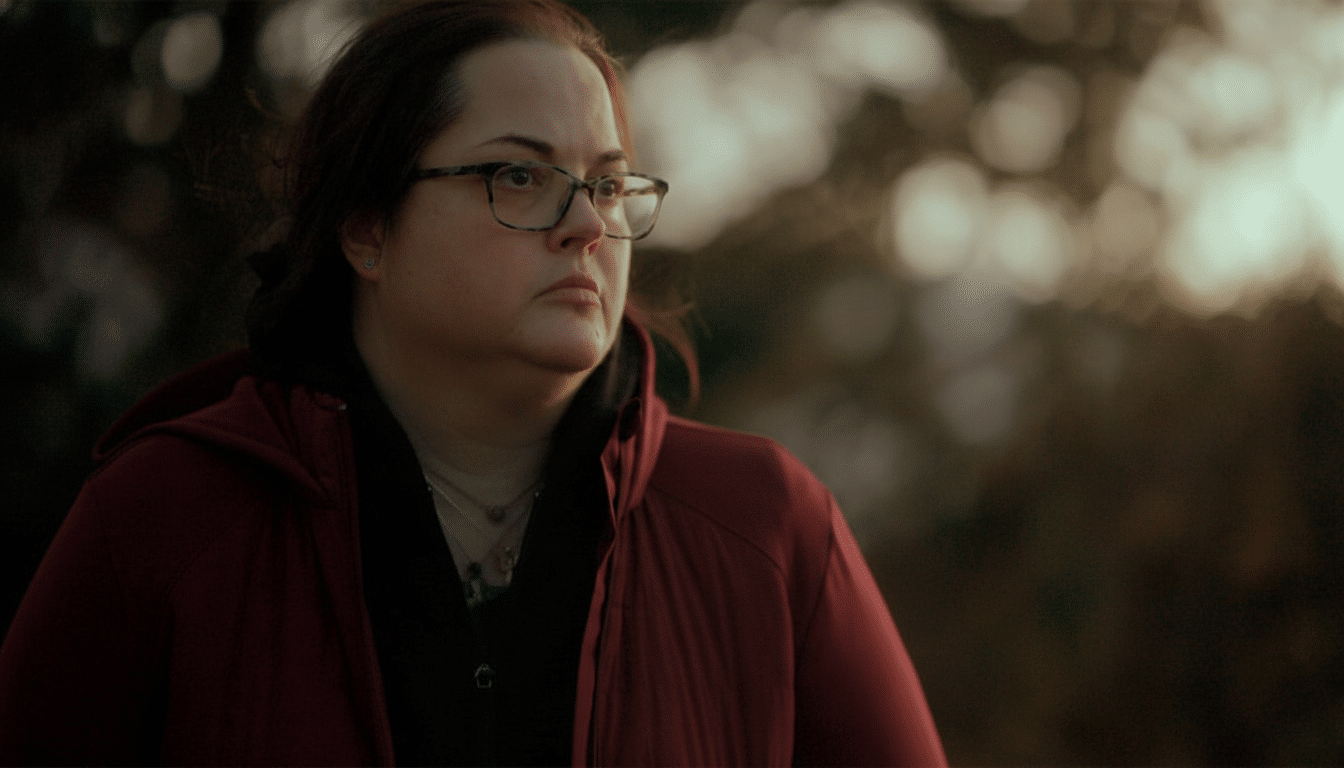 A woman with glasses and a red jacket looks to her right with a serious expression, against a bokeh background of soft outdoor light. Filename : womanred jacketoutdoor portrait .png