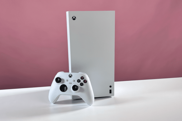 An Xbox Series S console and a white Xbox wireless controller are displayed on a white surface against a pink background .