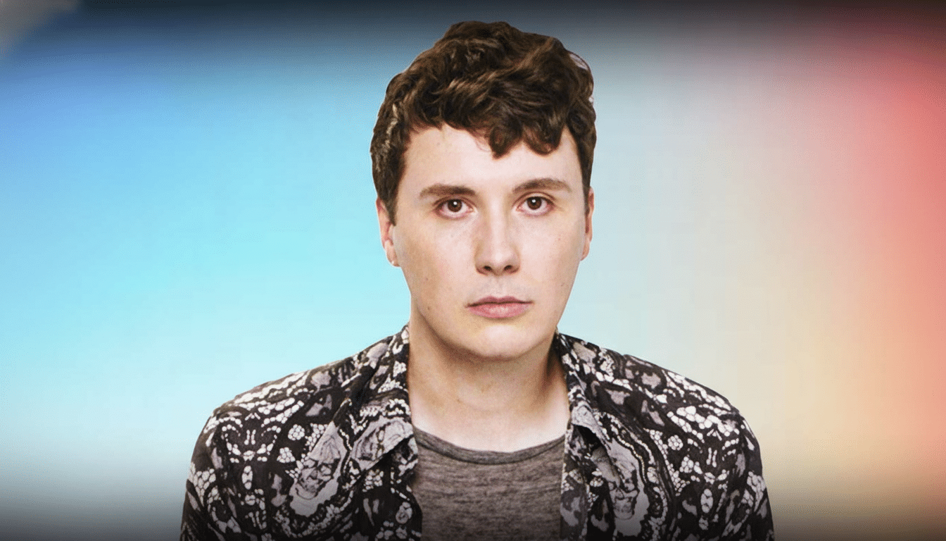 A young man with brown hair and a patterned shirt looking directly at the viewer , against a soft gradient background.