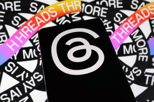 A smartphone displaying the Threads app logo, a white circular a symbol, against a background of white text on black reading THREADS and SAY MORE.