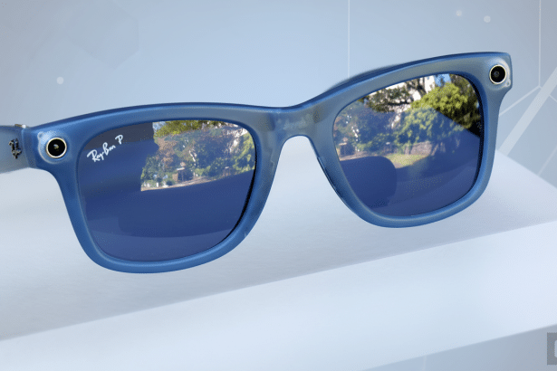 A pair of blue Ray-Ban Stories smart glasses displayed on a white surface , with a professional , soft gradient background in a 16 :9 aspect ratio . The reflections in the lenses show an outdoor scene.