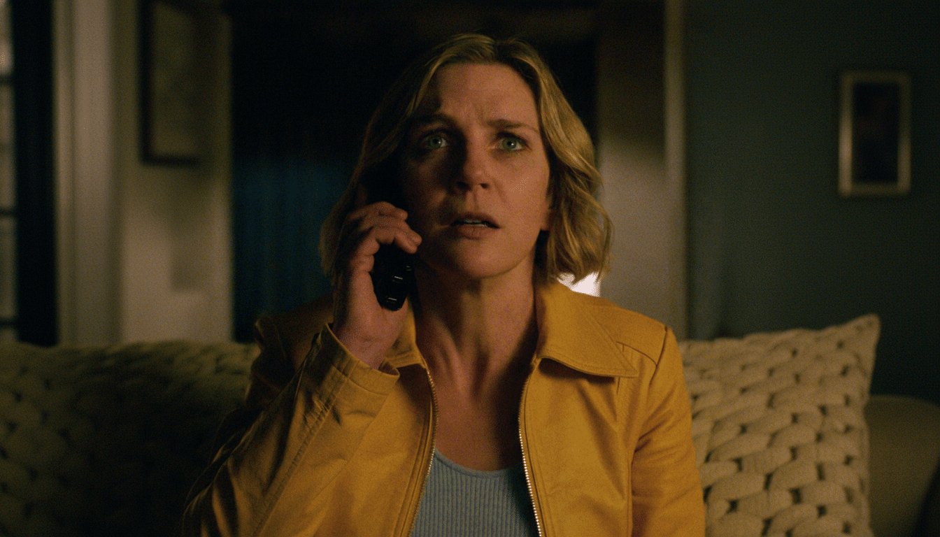 A woman with blonde hair and a yellow jacket holds a phone to her ear, looking surprised or concerned.