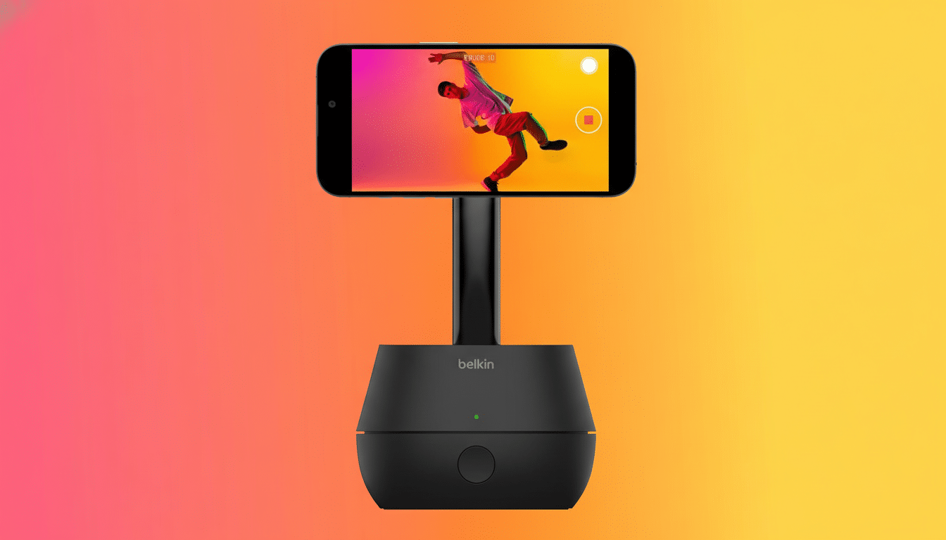 A black Belkin phone stand holding a smartphone horizontally, displaying a person dancing on its screen. The background is a gradient of orange and pink.