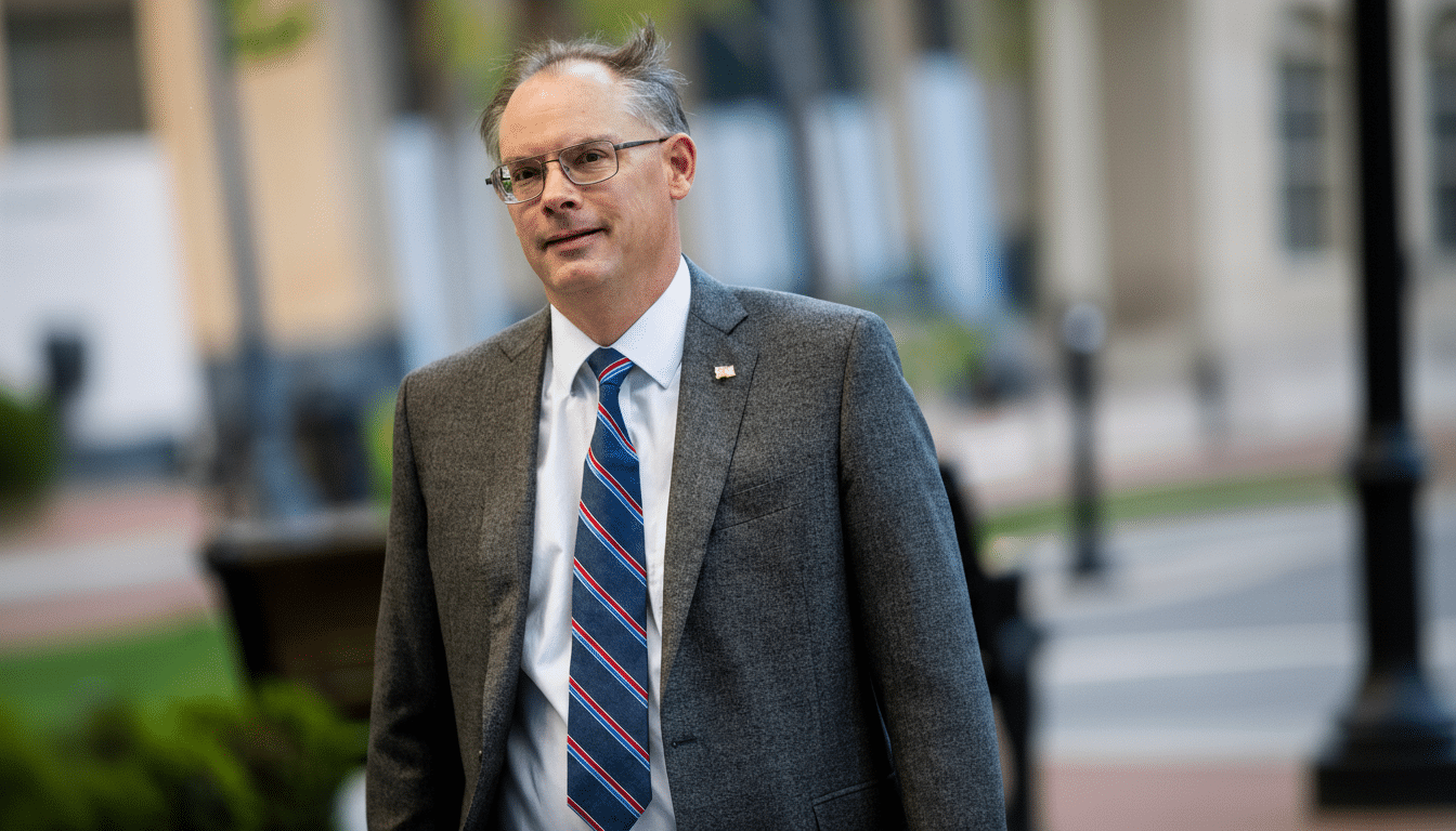 A man in a suit and tie with glasses looking forward.
