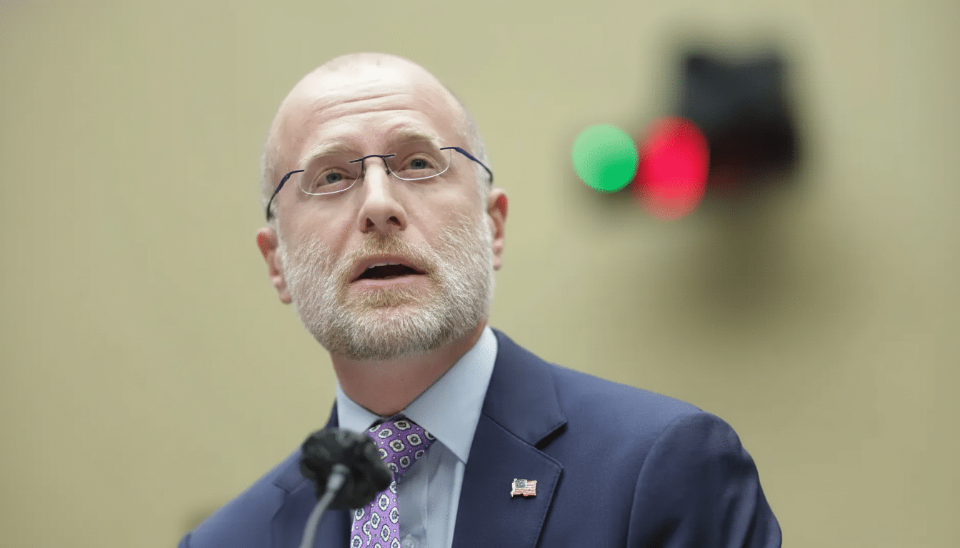 A man with a beard and glasses wearing a suit and tie, speaking into a microphone.