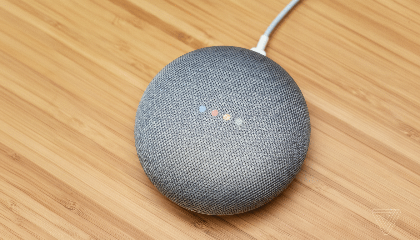 A gray Google Home Mini smart speaker with four colored indicator lights on its top surface, resting on a wooden surface.