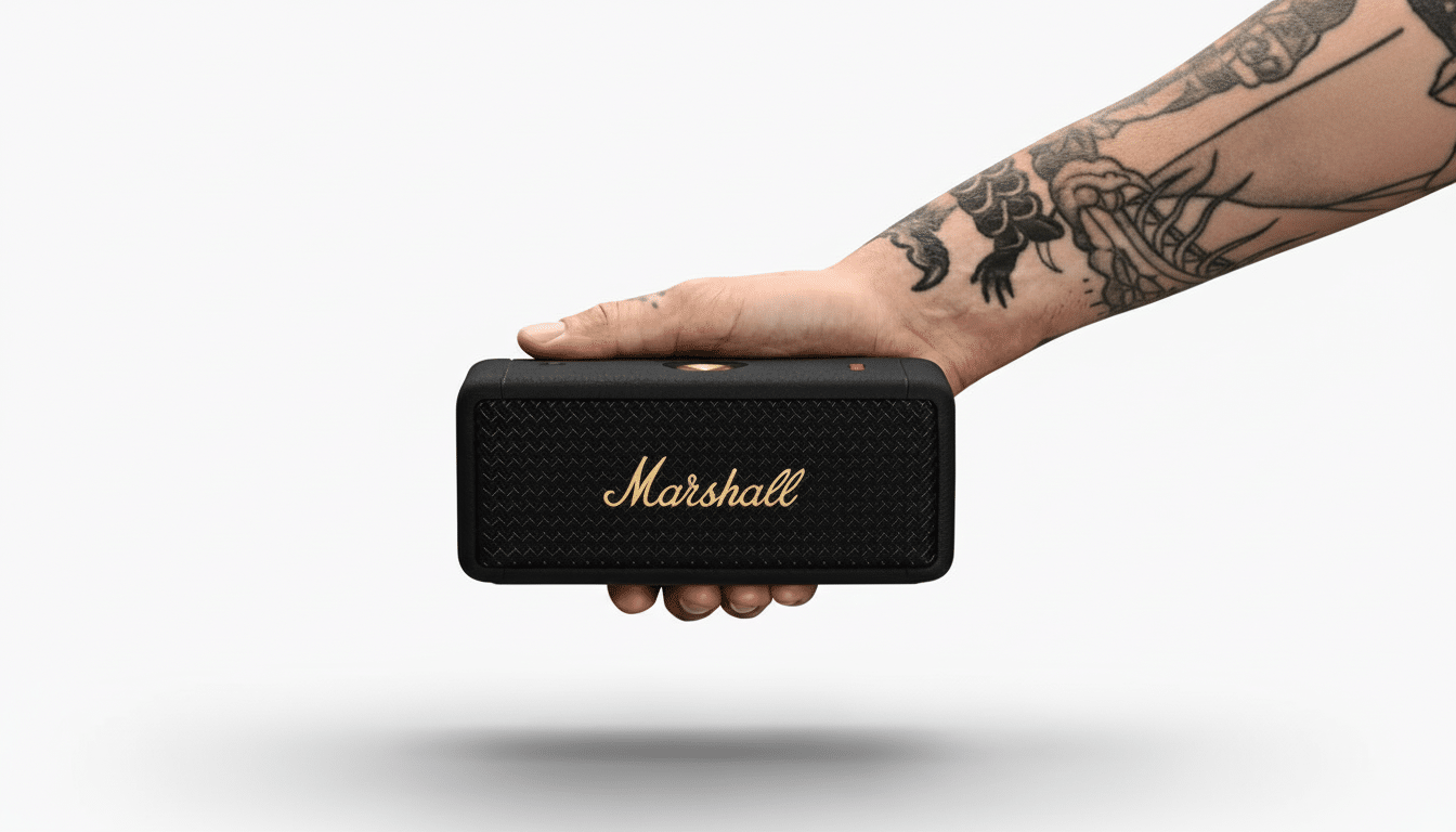 A hand with tattoos holding a black Marshall portable speaker with a gold logo, presented on a white background.