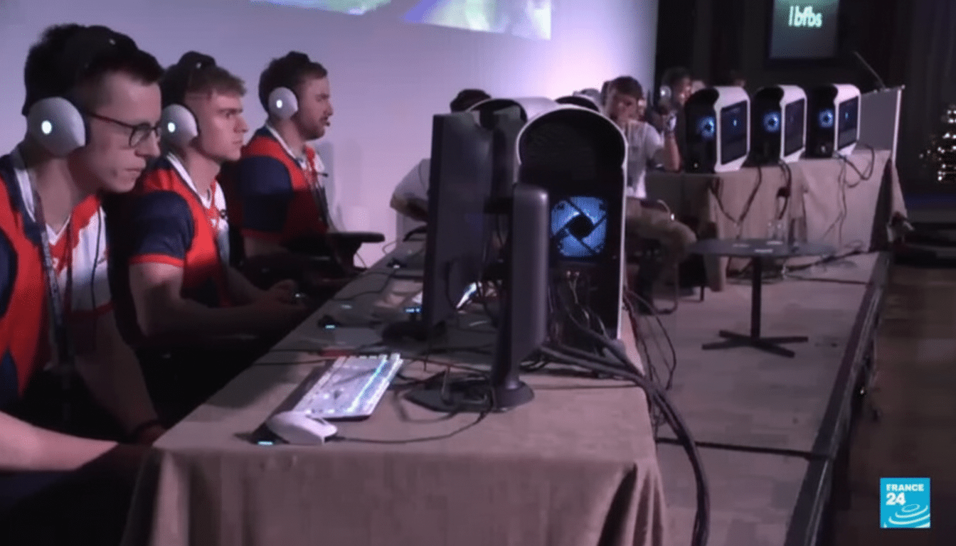 A group of young men wearing headphones are seated at a long table with computers, engaged in what appears to be an esports competition.