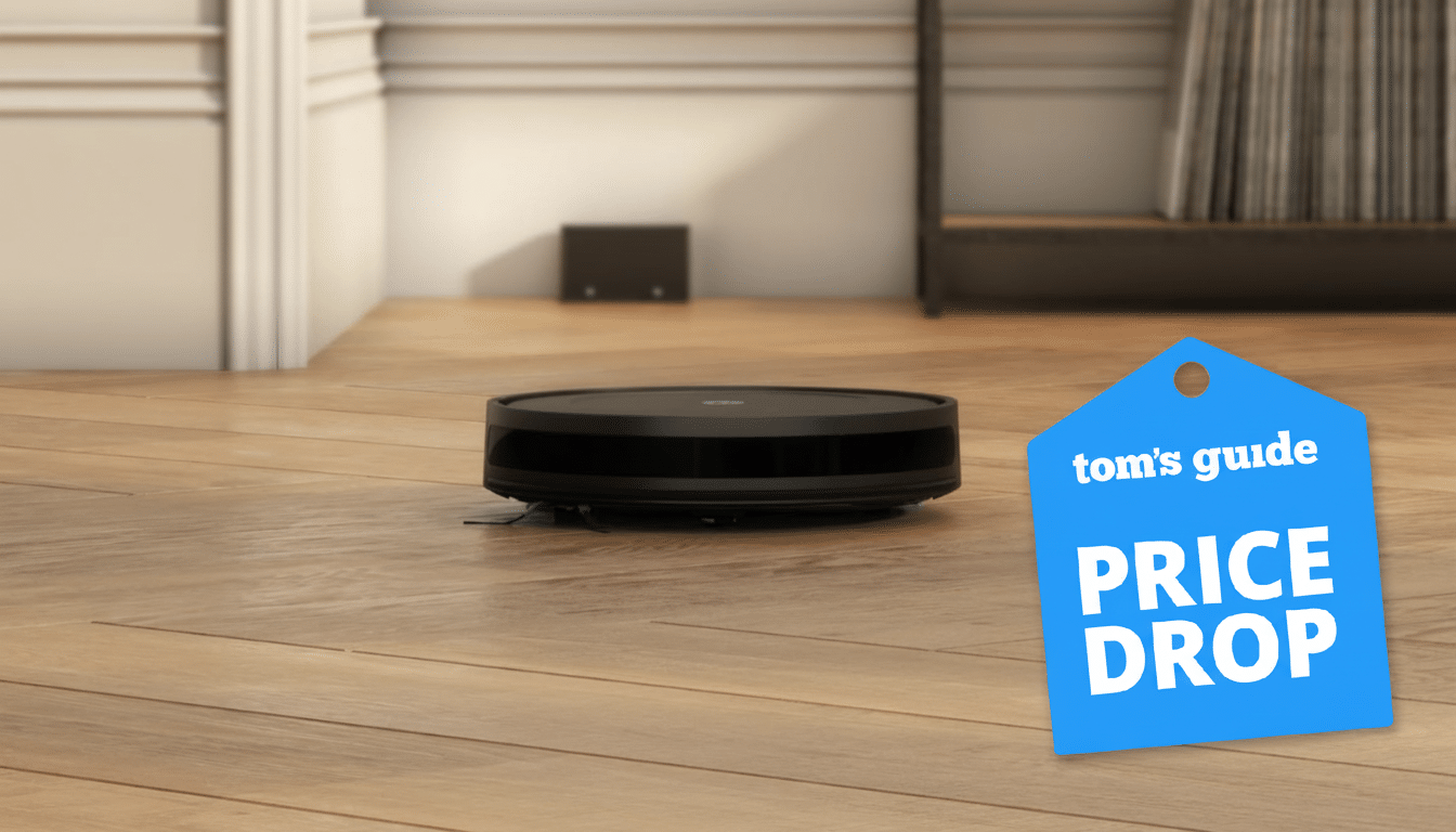 A black robotic vacuum cleaner on a wooden floor, with a blue Toms Guide Price Drop tag in the foreground.