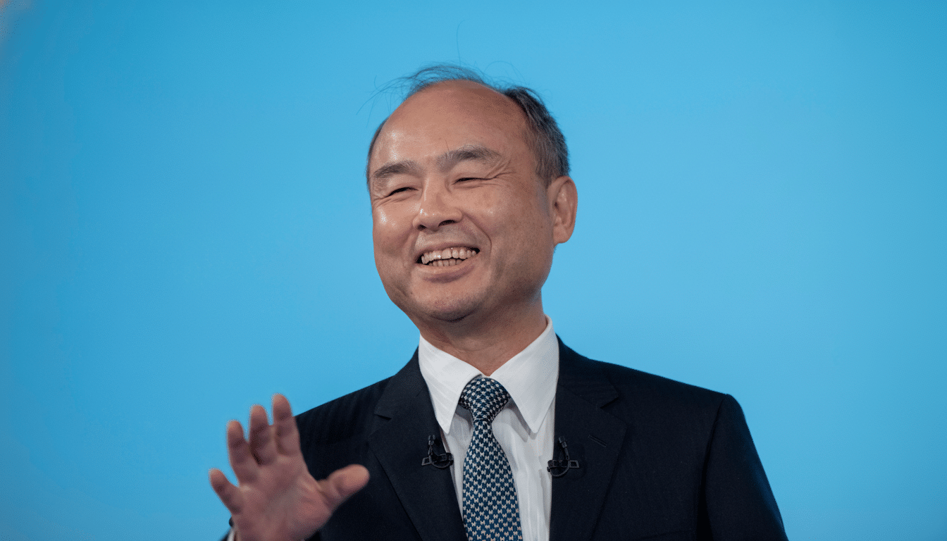 A man in a suit smiling and gesturing with his hand against a blue background.