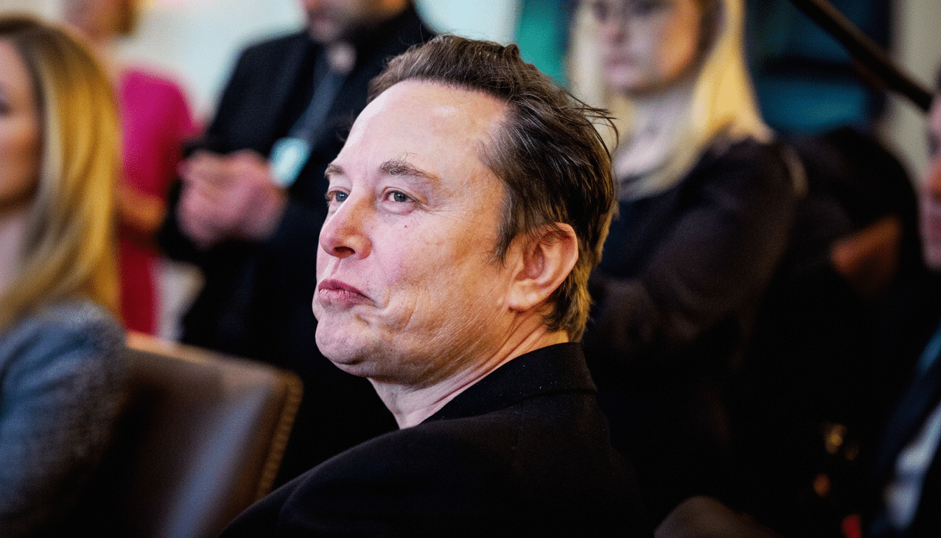 A man with short, dark hair and a black suit looks to the left with a slight frown, in a 16:9 aspect ratio.