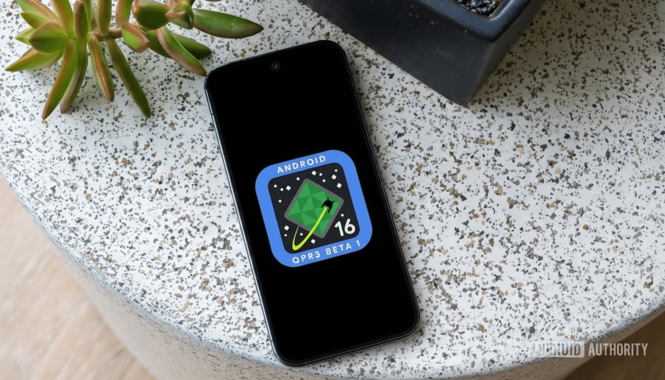 A smartphone displaying the Android QPR3 Beta 1 logo on its screen, placed on a speckled white surface next to a green succulent plant and a dark pot.