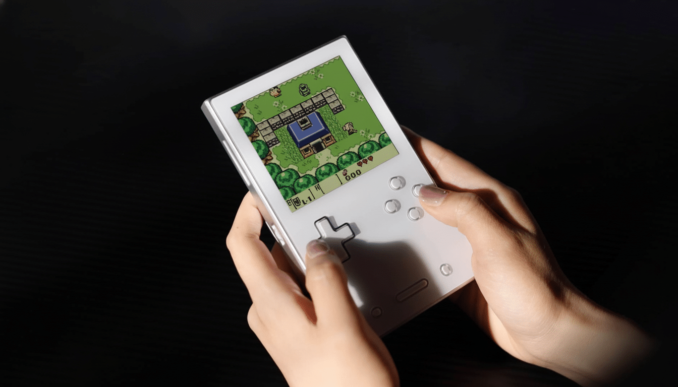 A persons hands holding a white handheld gaming device with a pixelated game displayed on its screen.