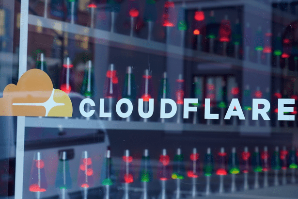 The Cloudflare logo and name are displayed on a glass window, with a blurred background of colorful lava lamps inside.