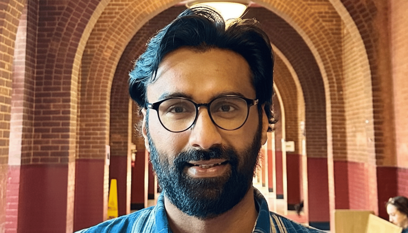 A man with a beard and glasses smiles at the camera, with a background of brick arches.