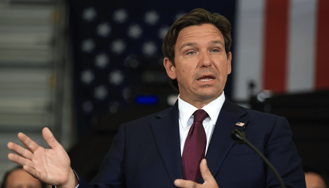 A man in a suit and tie speaking at a podium with an American flag in the background, resized to a 16:9 aspect ratio.