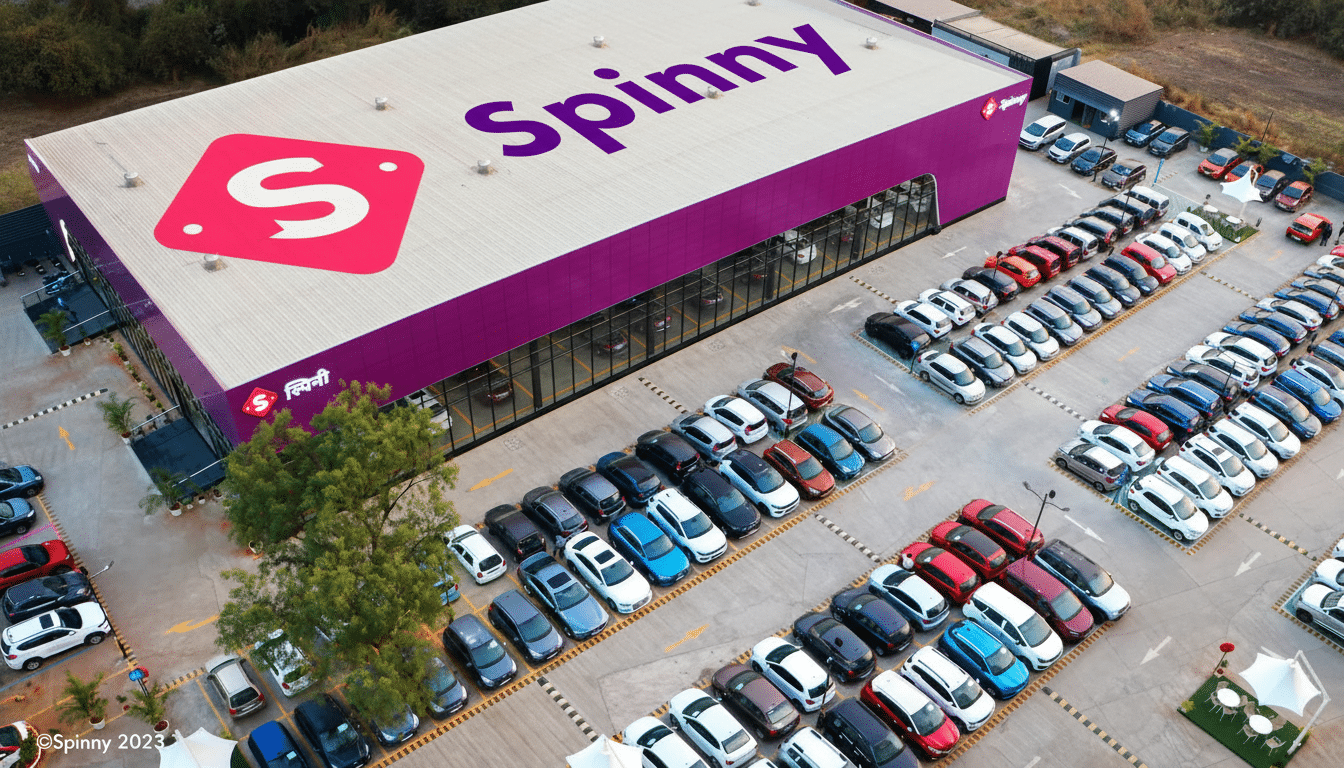 An aerial view of a Spinny car dealership with a large purple building and a parking lot full of cars.
