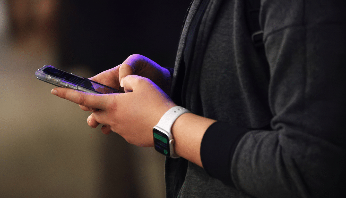 A persons hands holding a smartphone, with an Apple Watch on their left wrist, resized to a 16:9 aspect ratio.