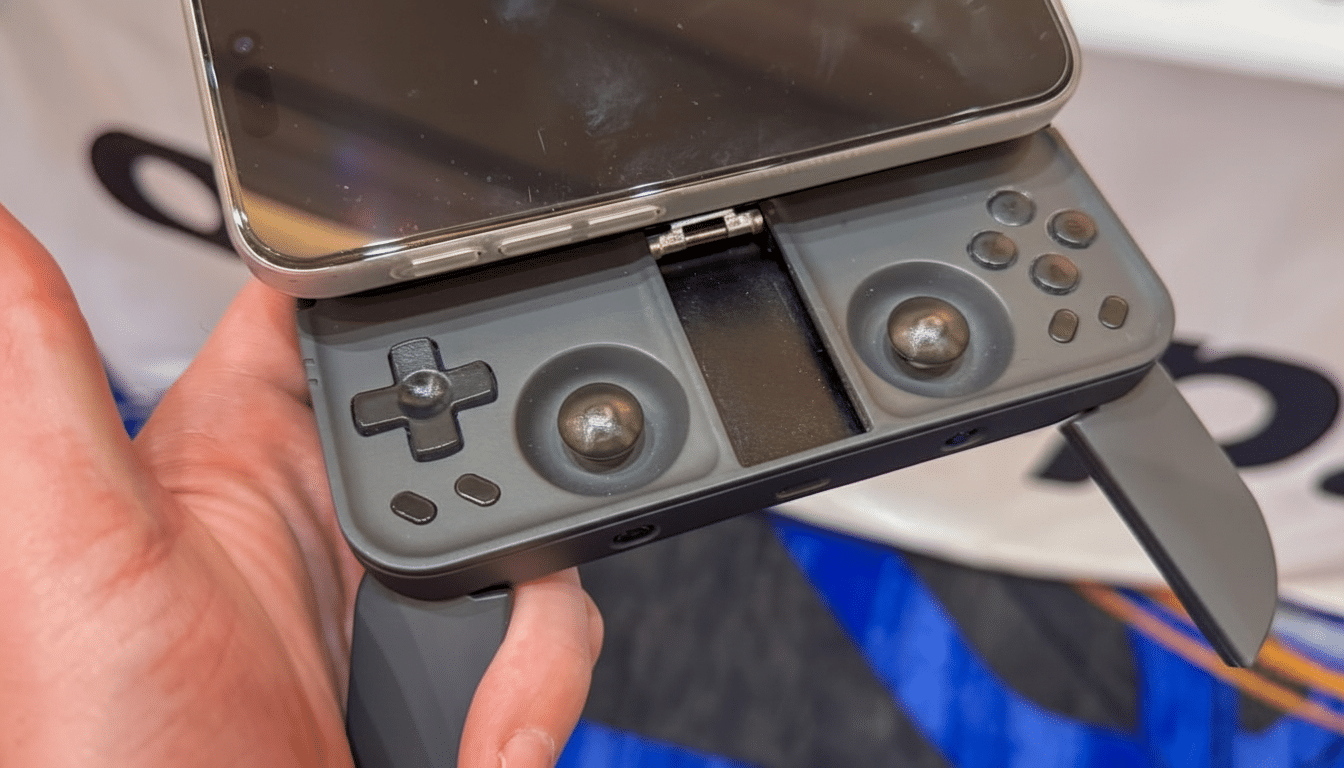 A hand holding a smartphone attached to a gray mobile gaming controller, resized to a 16:9 aspect ratio.