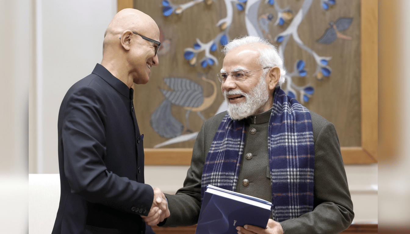 Two men, one with a bald head and glasses wearing a black suit, and the other with a white beard and glasses wearing a dark jacket and plaid scarf, shake hands and smile. The man in the jacket holds a blue book. A decorative wall hanging is visible in the background.