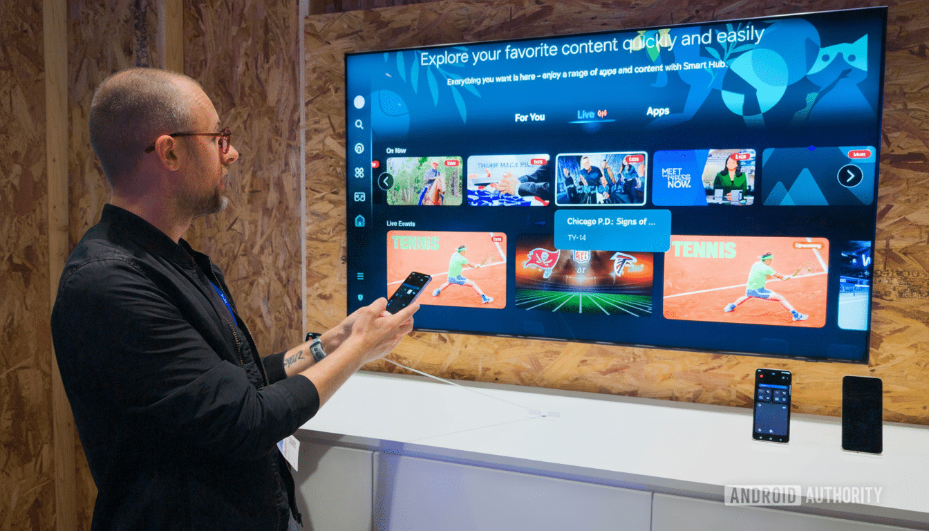 A man in glasses and a black jacket holds a smartphone, interacting with a large smart TV displaying various content options, including live events and apps. The TV is mounted on a wooden panel wall.