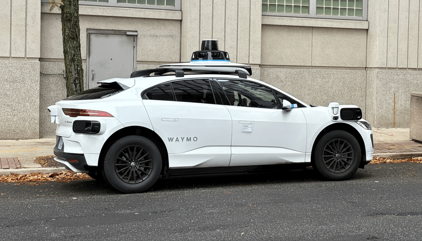 A white Waymo self-driving car parked on a street next to a building.