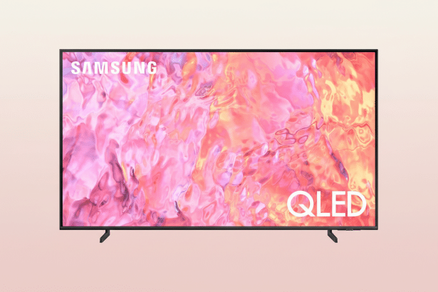 A Samsung QLED television with a vibrant pink and orange abstract image on its screen, set against a soft, light pink gradient background.