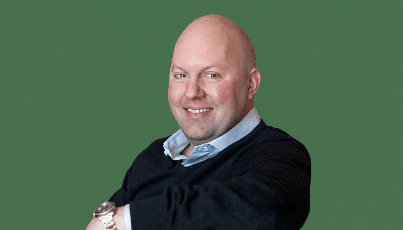 A smiling bald man in a dark sweater and light blue shirt, with a watch on his left wrist, against a solid green background.