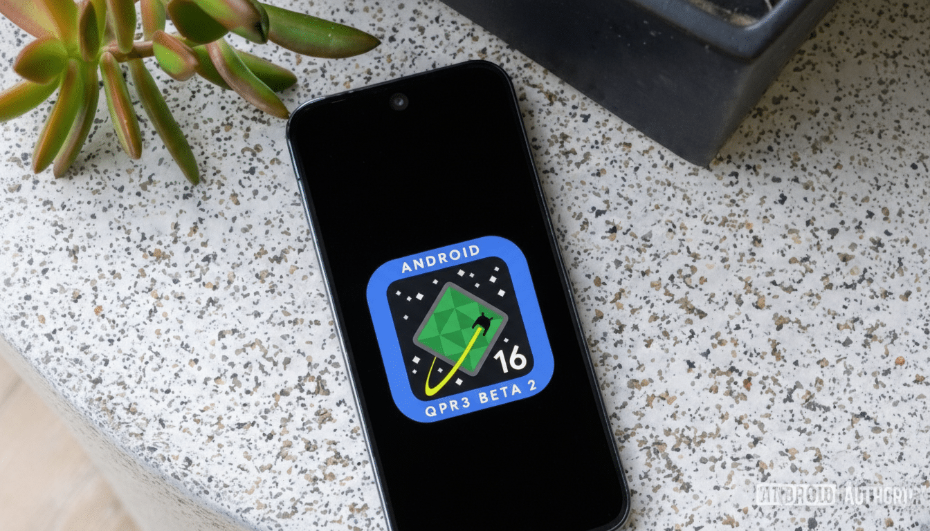 A smartphone displaying the Android 16 QPR3 Beta 2 logo on its screen, with a plant and a dark object in the background.