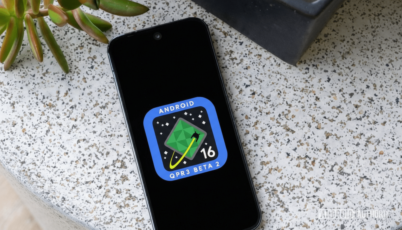 A smartphone displaying the Android 16 QPR3 Beta 2 logo on its screen, set against a speckled countertop with a plant in the background.