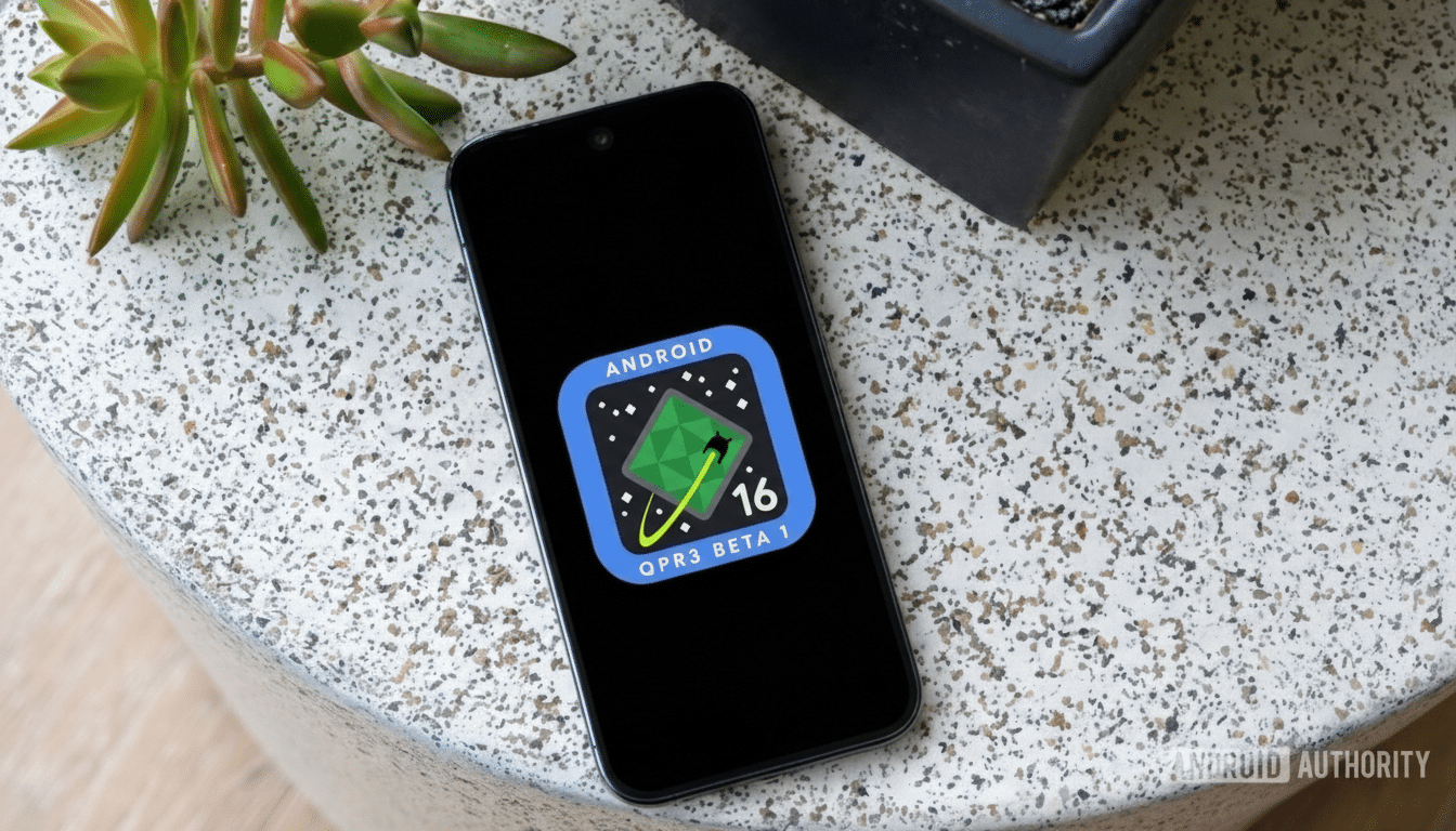 A smartphone displaying the Android QPR3 Beta 1 logo on its screen, set against a speckled light gray surface with a green succulent plant and a dark pot in the background.