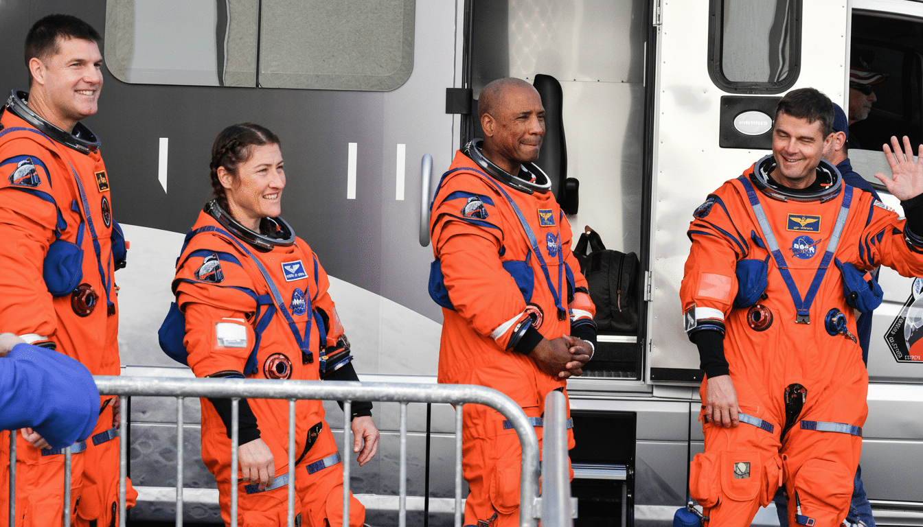 Four astronauts in orange flight suits stand outside a vehicle, with one waving.