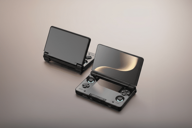 Two black handheld gaming devices with screens open, one facing forward and the other angled slightly away, on a smooth, gradient brown surface.