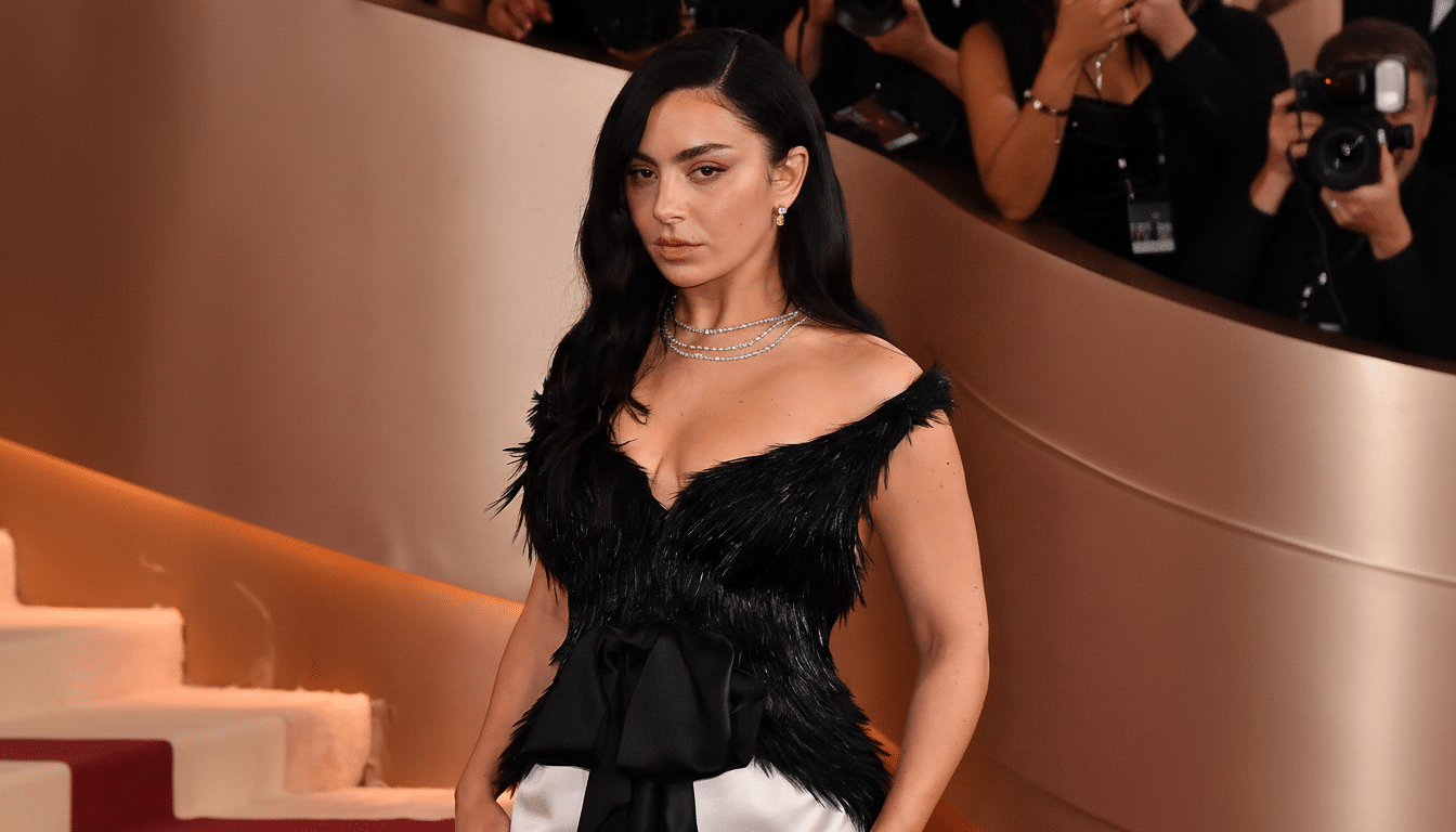 A woman with long dark hair wearing a black feathered top and white pants, standing on a red carpet with a blurred background of people and stairs.