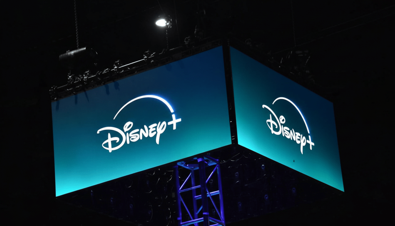 The Disney+ logo displayed on two large, illuminated screens hanging from a dark ceiling, with a metal truss structure visible below.