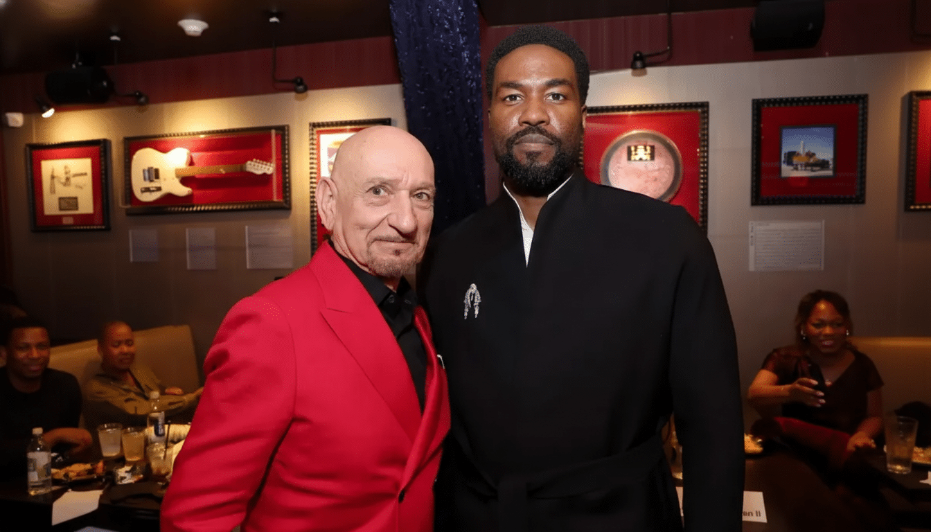 Two men, one in a red suit and the other in a black robe, stand side-by-side in a restaurant setting.