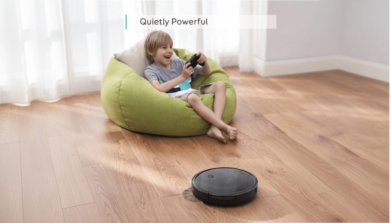 A young boy sitting in a green beanbag chair, playing a video game, while a black robotic vacuum cleaner operates on the wooden floor in front of him. The text Quietly Powerful is visible in the upper left corner.