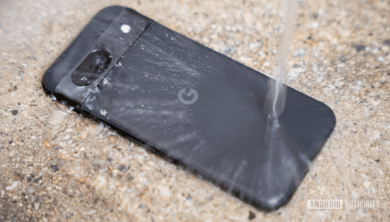 A black Google Pixel smartphone lying on a wet, textured surface with water streaming over its back, showcasing its water resistance.