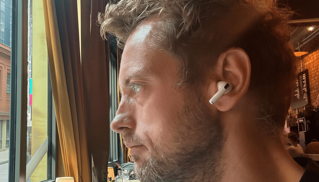 A man with an earbud in his right ear looks out a window.