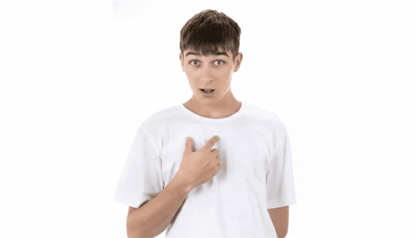 A young man in a white t-shirt points to himself with a surprised expression.