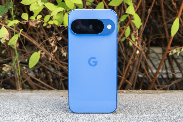 A blue Google Pixel phone standing upright on a concrete surface with a background of green leaves and brown branches.